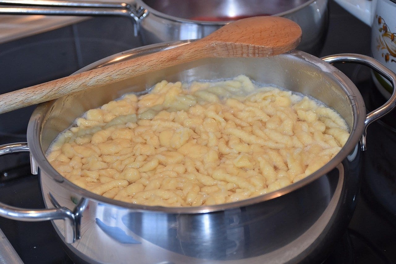 Frisch gegarte Spätzle schwimmen dicht an dicht an der Oberfläche eines Edelstahltopfs, darauf liegt ein Holzlöffel
